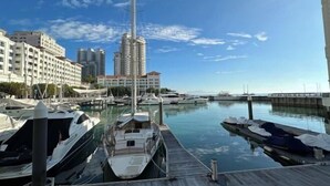 A marina with boats docked, a tall building in the background, and a clear sky. - Cozy Straits Quay Seafront Homestay (Tanjung Tokong)