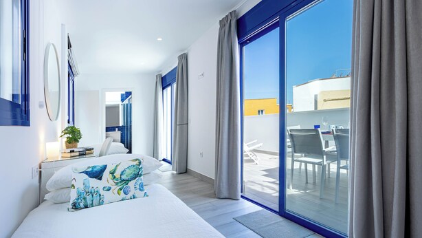 A modern hotel room with a large bed, a view of the terrace, and a bright, airy atmosphere.