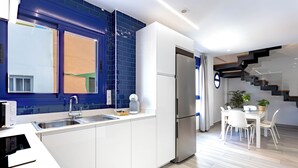 A modern kitchen with a built-in oven, a sink, and a refrigerator. There is a dining area with a table and chairs.