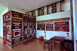 Zona de lavandería con varias lavadoras, una lista de precios y carteles informativos en la pared.