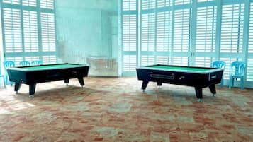 Two pool tables in a room with a patterned floor and large windows.