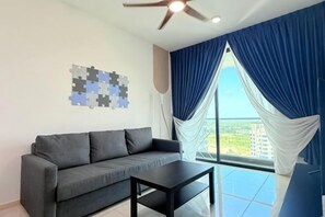 A modern living room with a grey sofa, a black coffee table, a ceiling fan, and a large window with blue curtains. - Macrolink 2B2R 7 pax Condo Medini near legoland (Iskandar Puteri)