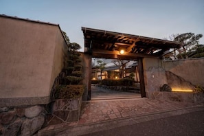 Perinteinen japanilaistyylinen sisäänkäynti, jossa on puinen pergola, kiviporras ja hyvin hoidettu puutarha.