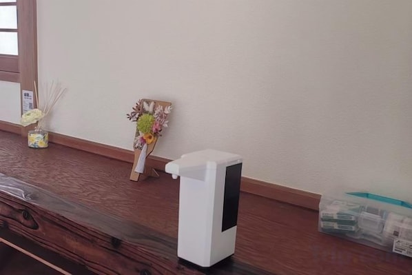 Una habitación con piso de madera, un purificador de aire blanco, un pequeño florero con flores secas y un cuadro en la pared.