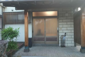 Una entrada japonesa tradicional con puertas correderas, un muro de piedra y un pequeño jardín.