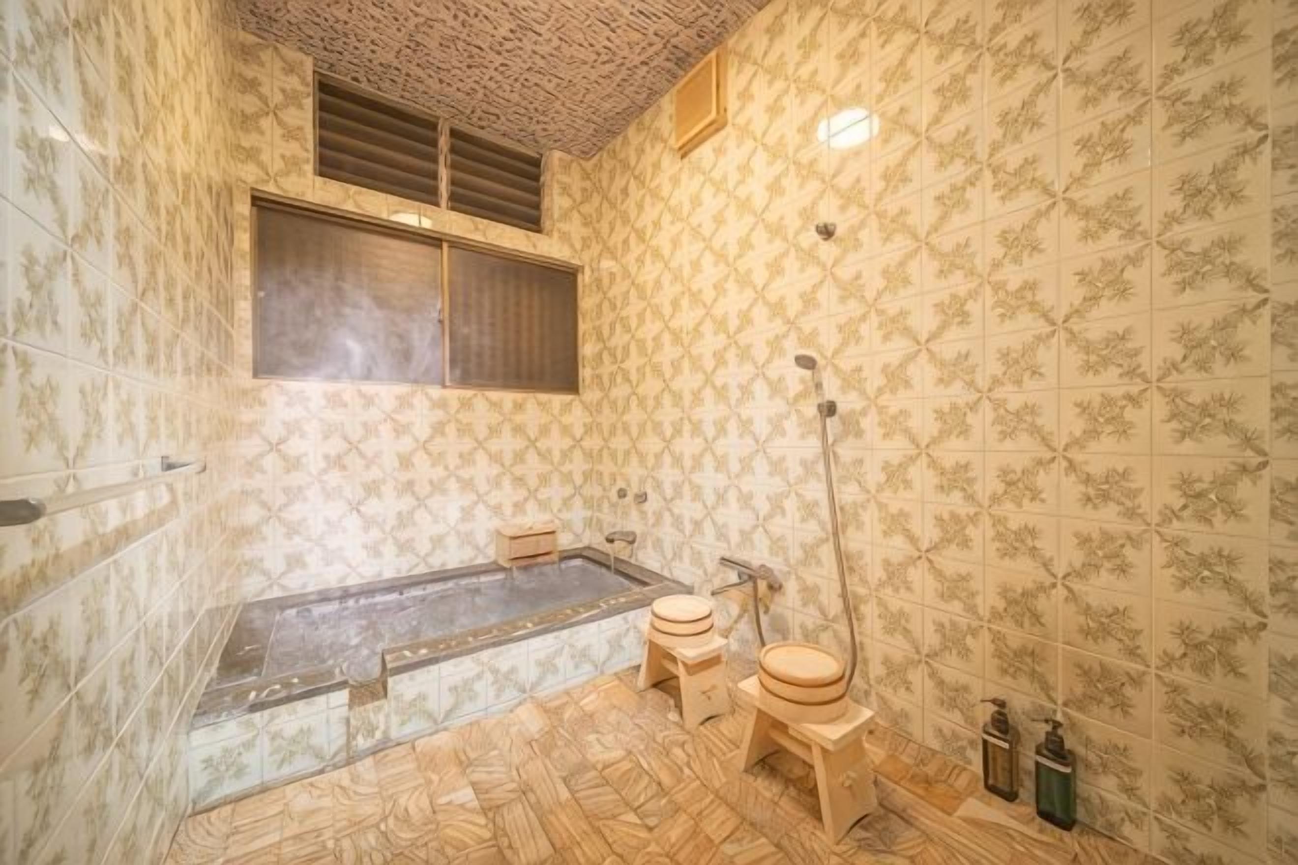 Un baño con bañera, dos taburetes, zona de ducha y una ventana.