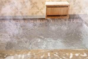 Una vasca idromassaggio con acqua che vi scorre al suo interno, una panca di legno e pareti in piastrelle.