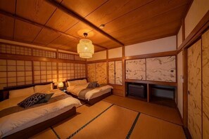 Perinteinen japanilainen huone, jossa on tatamimatto, kaksi sängyä tyynyineen, riippuvalaisin ja liukuvat ovet.