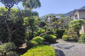 Un jardín ajardinado con arbustos y árboles variados, un sendero de grava y un edificio de estilo arquitectónico tradicional.