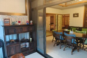Una habitación tradicional japonesa con suelo de tatami, una mesa de madera baja con sillas, y una puerta corredera que da a otra habitación.