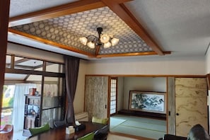 Una habitación tradicional japonesa con suelo de tatami, una mesa baja con cojines, una puerta corredera y un techo con diseño geométrico.