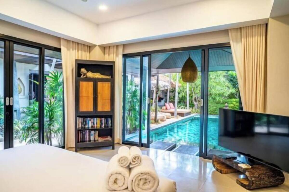 A modern bedroom with a large bed, a television, and a view of an outdoor swimming pool.