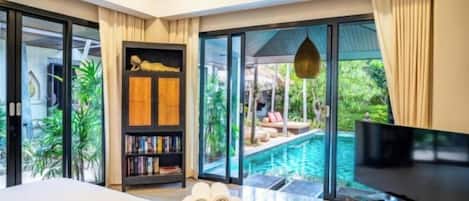 Un dormitorio moderno con una cama grande, una televisión y vistas a una piscina exterior.