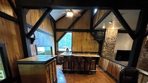 Interior de madera con barra, un pilar de piedra y vistas al exterior por una ventana.