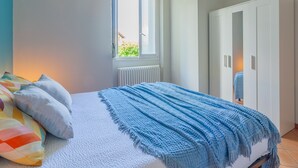 Ein Schlafzimmer mit Bett, Fenster, Heizkörper und Kleiderschrank.