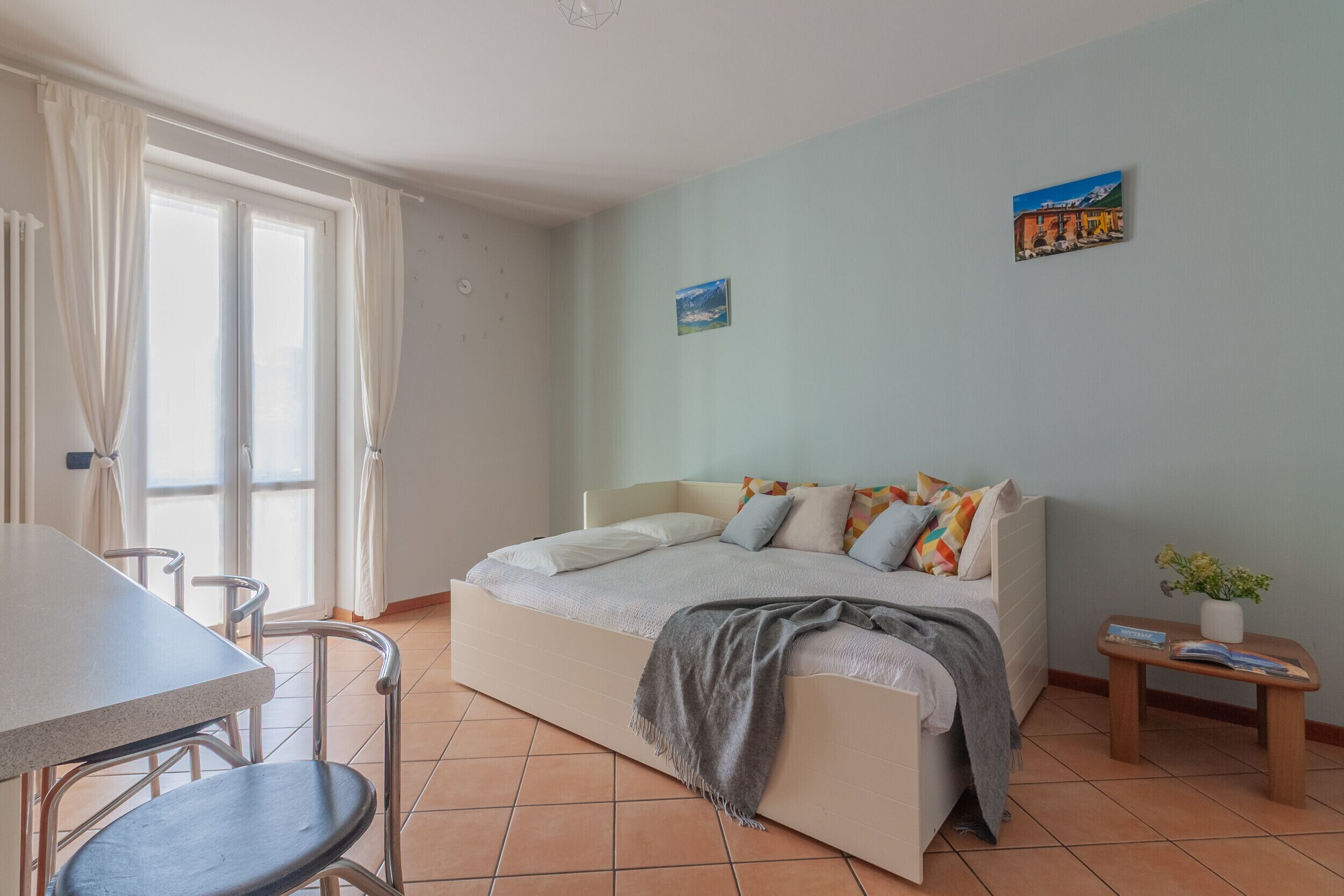 Une chambre à coucher comprenant un lit, une table à manger, des chaises, une petite table avec un vase et un mur orné de deux tableaux.