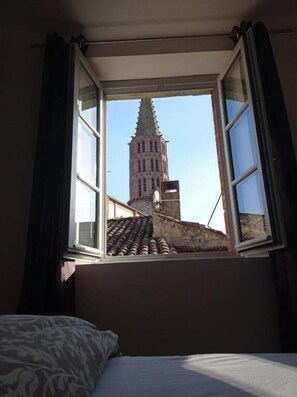 A room with an open window overlooking a historic building with a pointed roof. - Les Coulisses du Chteau (Negrepelisse)