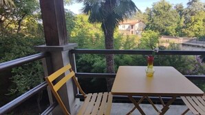 Un balcó amb una taula i dues cadires, amb vista a un jardí exuberant i una zona residencial.