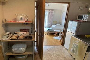 A compact kitchen with a microwave, kettle, and various kitchenware on shelves.