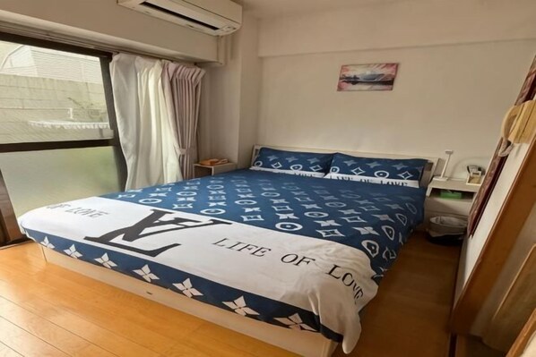 A bedroom with a bed, a nightstand, a window with curtains, and a wall-mounted air conditioner.