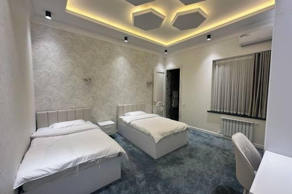 Ein modernes Hotelzimmer mit zwei Betten, einem Schreibtisch, einem Stuhl, einem Heizkörper und einem Fenster mit Vorhängen.