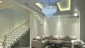 A modern living room with a sectional sofa, a coffee table, a chandelier, and a staircase with white railings. - yuelai hotel (Tashkent)