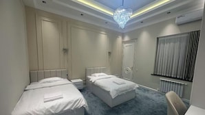 A hotel room with two beds, a chandelier, a radiator, and a window with blinds. - yuelai hotel (Tashkent)