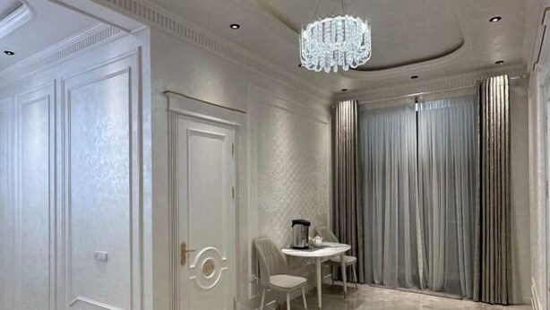 A room with a marble floor, a chandelier, a table with chairs, and a door with a circular handle. - yuelai hotel (Tashkent)