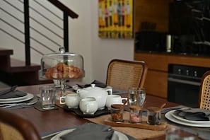 A dining table set with plates, glasses, a teapot, a glass of water, and a bread basket. - Tatkala Villa (Bali)