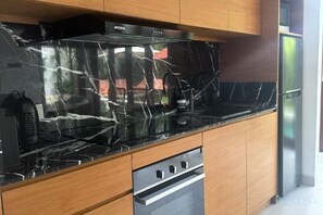 A kitchen with a black marble countertop, wooden cabinets, and stainless steel appliances. - Tatkala Villa (Bali)