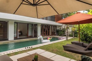 A modern pool area with a swan float, lounge chairs, and umbrellas. - Tatkala Villa (Bali)