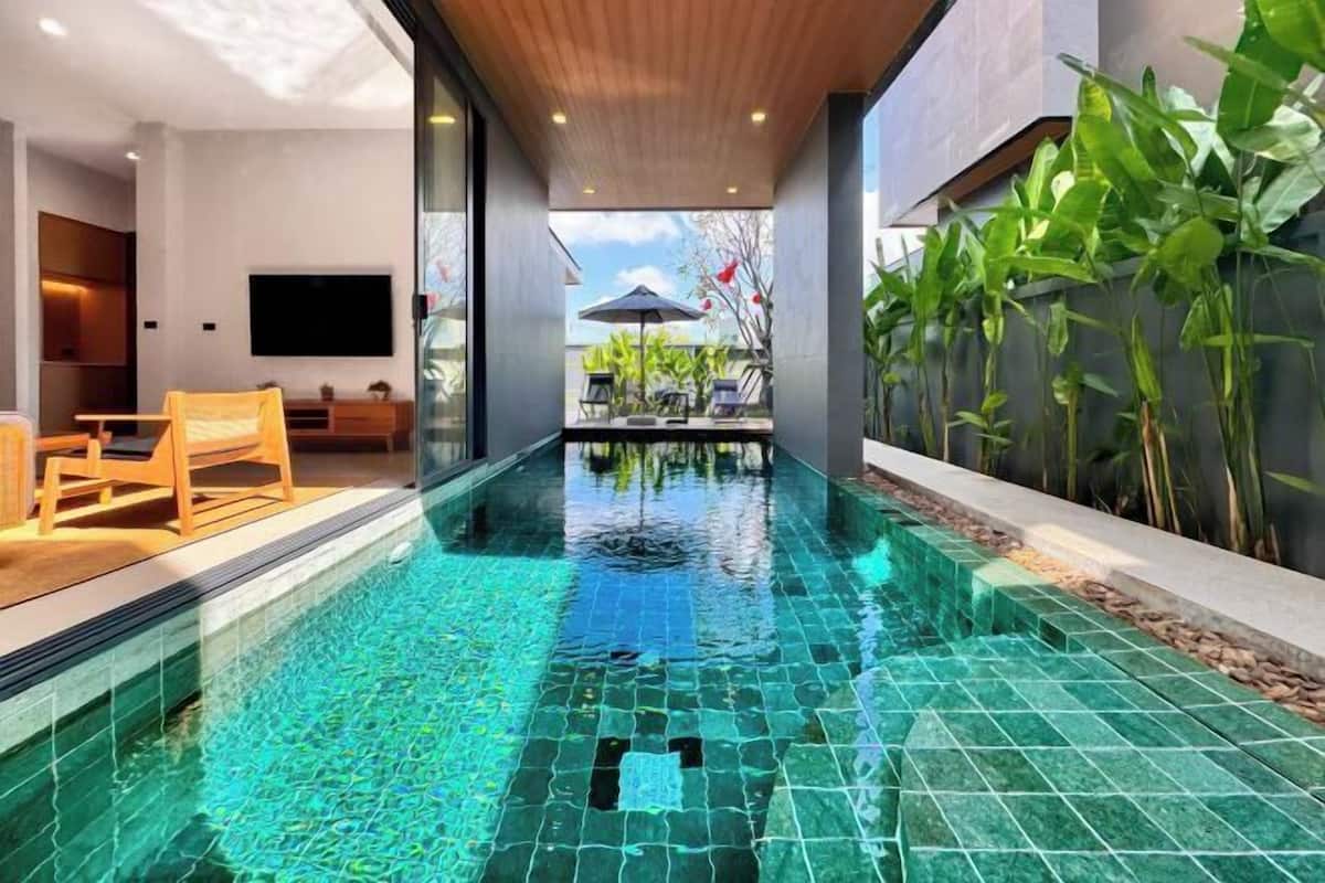 Una piscina interna moderna con acqua cristallina, sedute a terrazza in legno e un grande schermo televisivo.