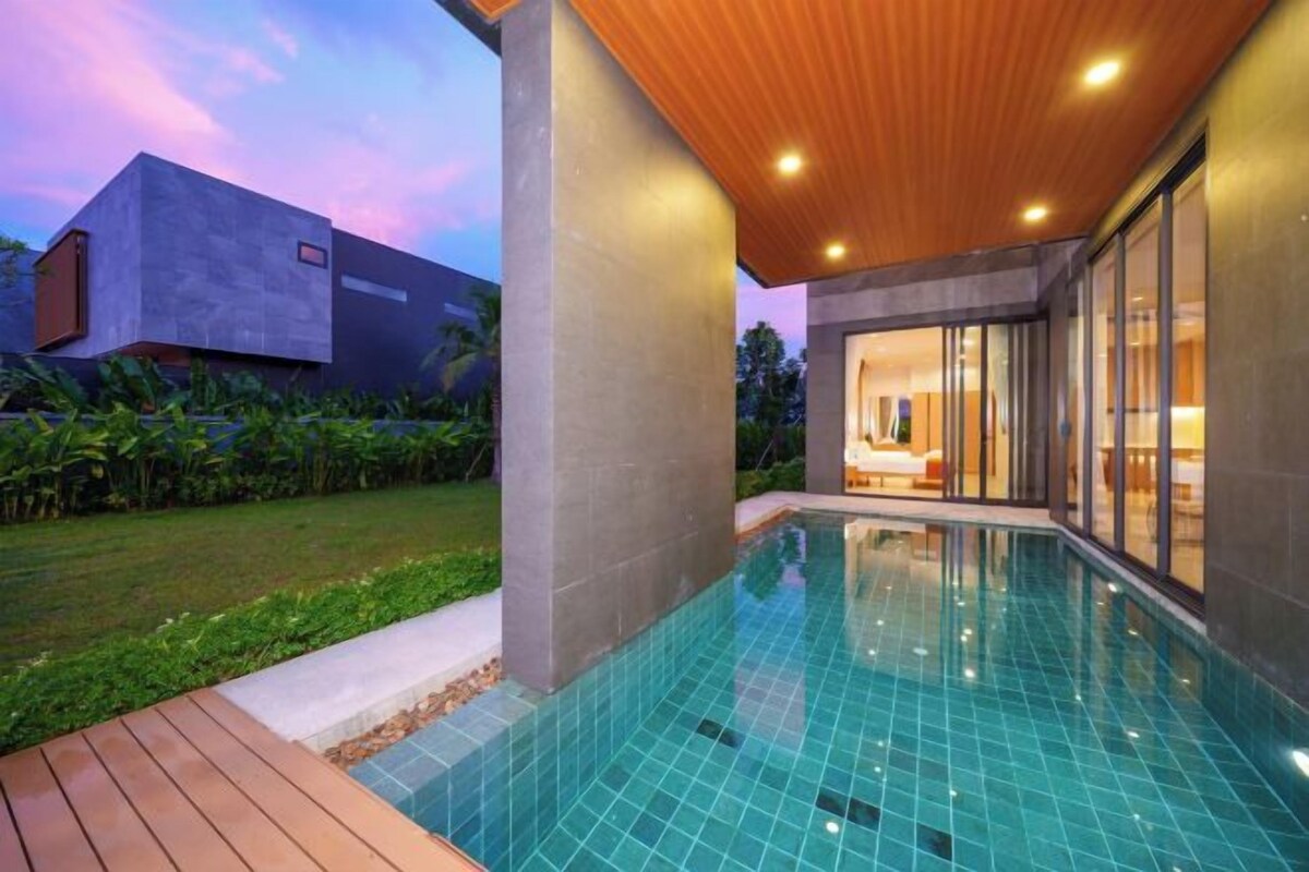 A modern pool area with a wooden deck, a concrete structure, and a view of a house.