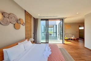 Una habitación de hotel moderna con una cama grande, un balcón con puerta de vidrio y una zona de estar con mesa y sillas.