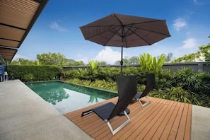 Zona junto a la piscina con muelle de madera, una silla de descanso, una sombrilla y una vista despejada de la piscina.