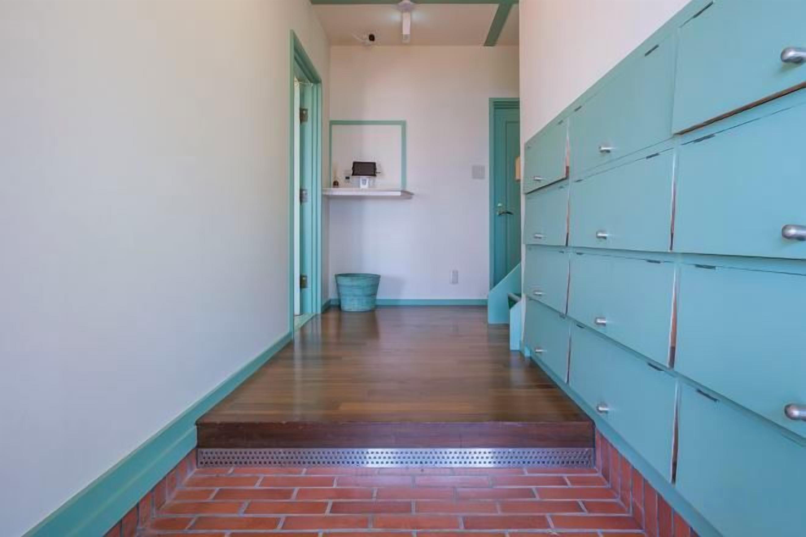 A hallway with lockers, a trash bin, and a shelf with a mirror.