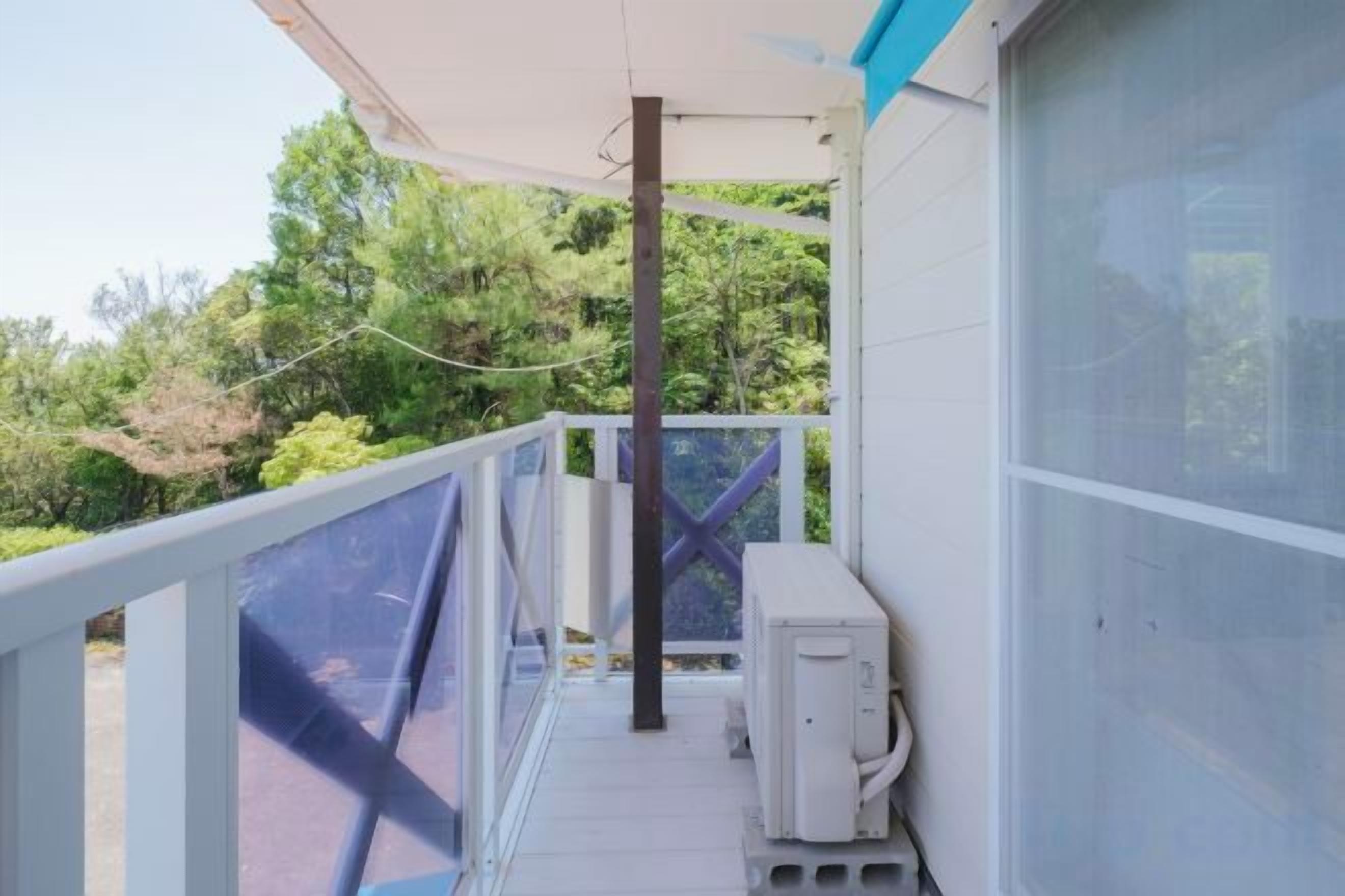 Un balcon avec une balustrade blanche, un climatiseur blanc et une vue sur la verdure.