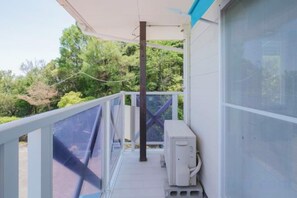 A balcony with a white railing, a white air conditioning unit, and a view of greenery. - NOSTALGIA NASA (Kaiyo)