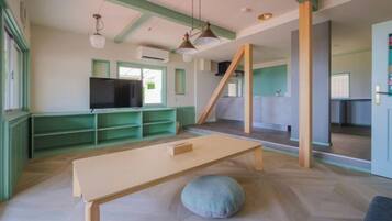 Una stanza con televisione, un tavolo di legno e un pouf.