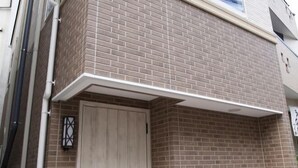 Een hoek van een gebouw met een bakstenen gevel, een witte deur en een klein raam met decoratieve lijst.