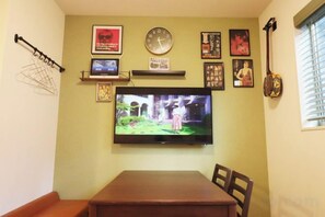 A dining area with a television mounted on the wall, a clock, and various framed pictures. - HAMA HILLS Shinjuku ANNEX (Tokyo)