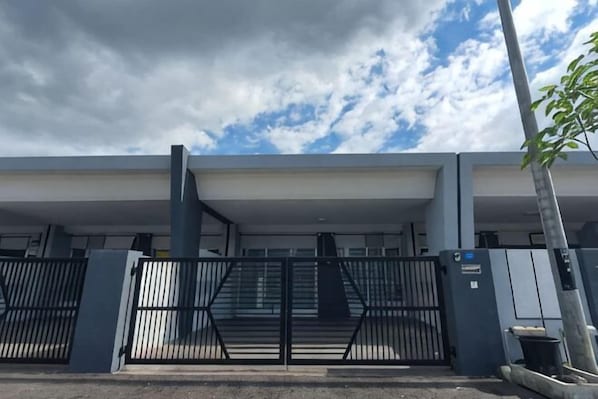 A gated entrance to a building with a covered walkway and a tree in the foreground. - PoloStay Landed House 4 Room for 10 pax (Ipoh)