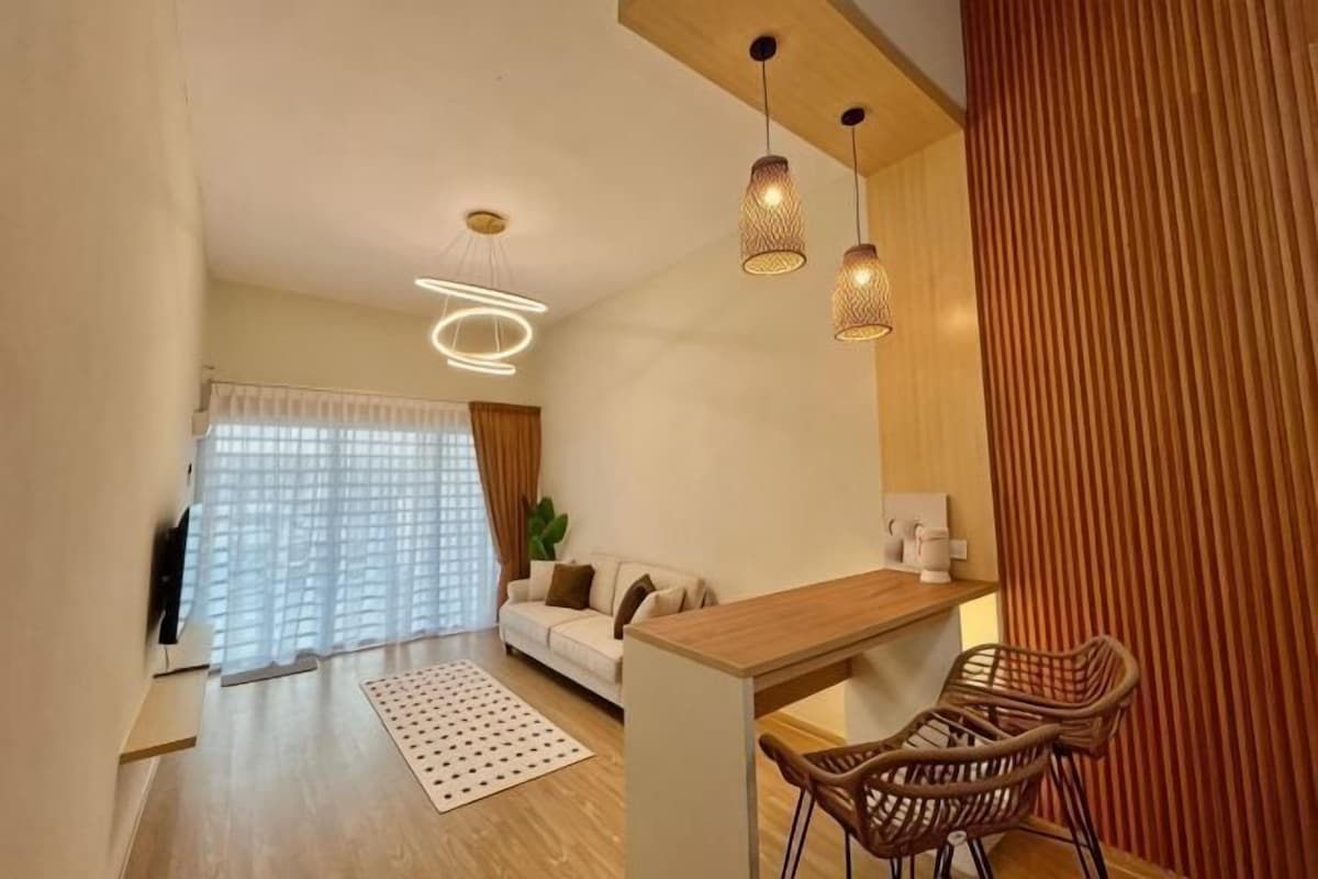 A modern living room with a sofa, a dining area with chairs, and a kitchen counter.