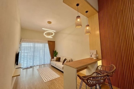 A modern living room with a sofa, a dining area with chairs, and a kitchen counter.