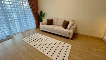 A living room with a beige sofa, a patterned rug, and a large window with curtains.