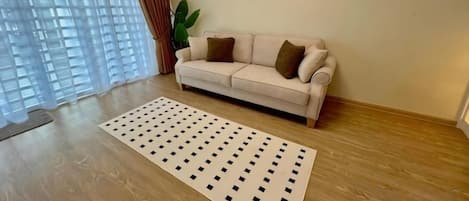 A living room with a beige sofa, a patterned rug, and a large window with curtains.
