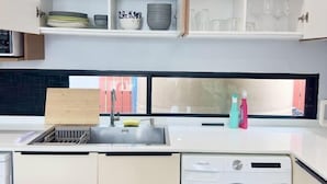 Une cuisine moderne équipée d’un lave-vaisselle intégré, d’un évier avec un égouttoir et d’une fenêtre donnant sur un immeuble rouge.