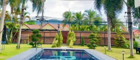 A swimming pool with a clear blue water surface, surrounded by a well-maintained lawn and palm trees.
