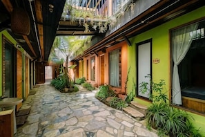 A narrow stone-paved corridor with wooden benches, potted plants, and a green building with windows and doors. - The Hill Sapa (TT. Sa Pa)