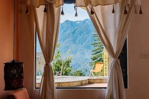 A room with a view of mountains through curtains, a small table, and a chair outside. - The Hill Sapa (TT. Sa Pa)